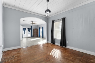 Empty room featuring arched walkways, healthy amount of natural light, wood-type flooring, and a ceiling fan