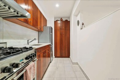 Kitchen with extractor fan, stainless steel appliances, light tile patterned floors, brown cabinets, and light stone counters