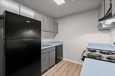 Kitchen featuring light countertops, gray cabinets, a sink, light wood-style floors, and black appliances