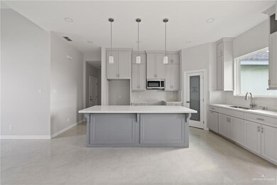 Kitchen featuring stainless steel microwave, a sink, a kitchen island, decorative light fixtures, and baseboards