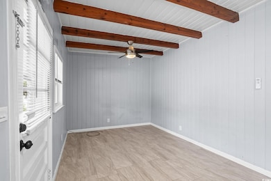 Empty room featuring wooden walls, a ceiling fan, and a wood ceiling with exposed beams