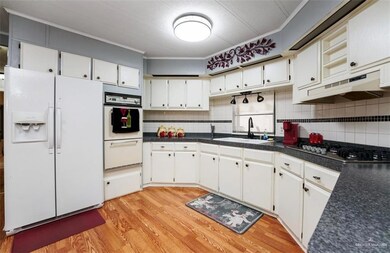 Kitchen featuring light hardwood / wood-style flooring, crown molding, stainless steel gas cooktop, and white refrigerator with ice dispenser