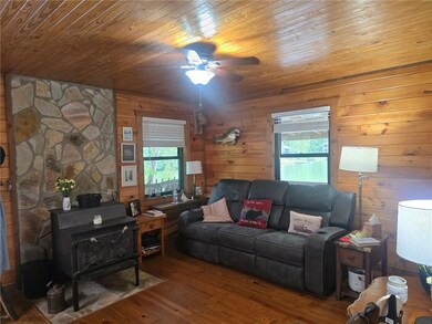 Living area with wood ceiling, a wood stove, hardwood / wood-style floors, a ceiling fan, and wooden walls