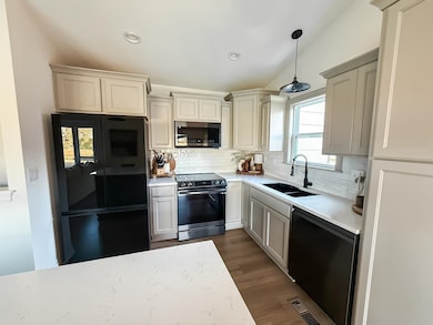 Kitchen with black appliances, decorative backsplash, decorative light fixtures, dark wood-style flooring, and light stone countertops