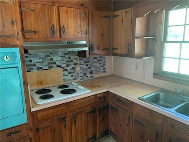 Kitchen with under cabinet range hood, white electric cooktop, decorative backsplash, and brown cabinetry