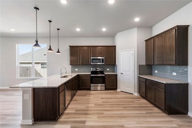 Kitchen with dark brown cabinets, light stone counters, appliances with stainless steel finishes, hanging light fixtures, and a peninsula