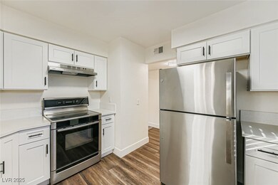Kitchen with white cabinetry, stainless steel appliances, dark wood finished floors, under cabinet range hood, and light stone countertops