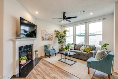 Living room featuring a ceiling fan, wood finished floors, fireplace with quartz surround and hearth. Lots of natural light and views of the outdoors.