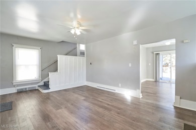Unfurnished living room with hardwood / wood-style floors, a ceiling fan, stairs, and baseboard heating