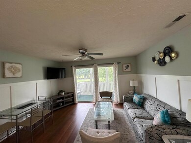 Living area featuring a wainscoted wall, a decorative wall, dark wood finished floors, a textured ceiling, and ceiling fan