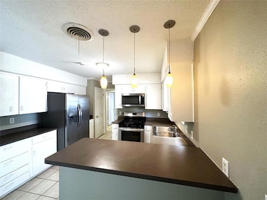 Kitchen featuring pendant lighting, appliances with stainless steel finishes, a peninsula, white cabinets, and a textured ceiling