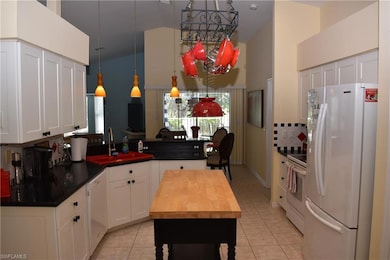 Kitchen with white appliances, sink, decorative light fixtures, light tile patterned flooring, and white cabinetry