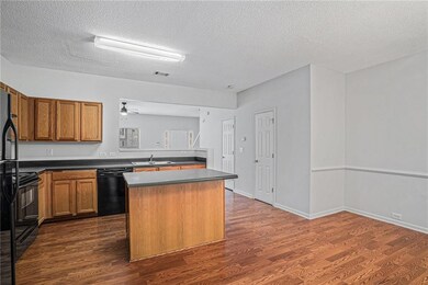 Kitchen featuring brown cabinets, dark countertops, dark wood-style flooring, black appliances, and a textured ceiling