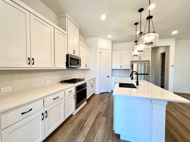 Kitchen with an island with sink, a sink, backsplash, appliances with stainless steel finishes, and dark wood-style flooring