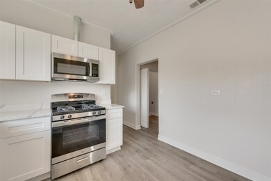 Kitchen featuring appliances with stainless steel finishes, white cabinetry, light wood-type flooring, light stone countertops, and a ceiling fan