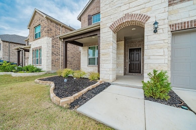 Doorway to property featuring stone siding, brick siding, covered porch, a lawn, and a garage