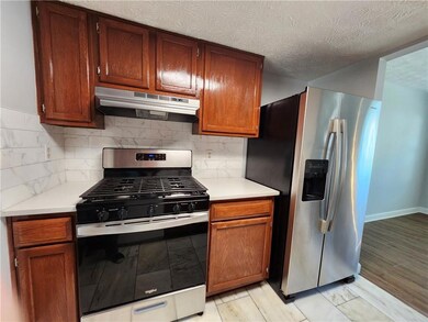 Kitchen with stainless steel appliances, under cabinet range hood, light countertops, and tasteful backsplash