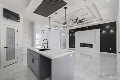 Kitchen with sink, hanging light fixtures, a tray ceiling, gray cabinets, and a kitchen island with sink