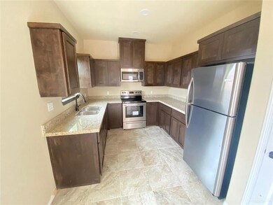 Kitchen featuring light stone counters, dark brown cabinetry, stainless steel appliances, and a sink