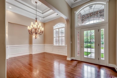 Foyer with crown molding, hardwood / wood-style floors, a chandelier, a tray ceiling, and a wainscoted wall