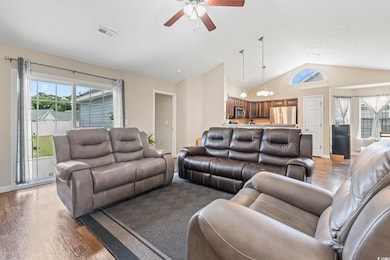 Living area with vaulted ceiling, light wood-style flooring, a ceiling fan, and a chandelier
