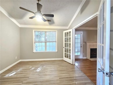 Unfurnished room with french doors, light wood-style flooring, crown molding, a ceiling fan, and a textured ceiling