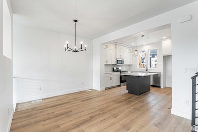 Kitchen with white cabinets, a chandelier, pendant lighting, stainless steel appliances, and light wood-type flooring