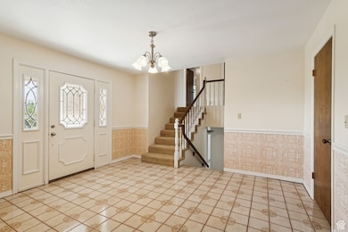 Entrance foyer with a wainscoted wall, stairway, a chandelier, and light tile patterned floors