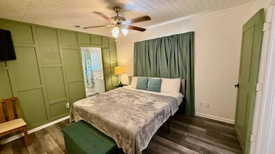 Bedroom featuring a decorative wall, dark wood-type flooring, ceiling fan, ensuite bath, and wooden ceiling