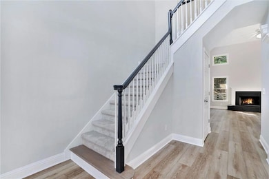 Stairway with wood finished floors, a warm lit fireplace, a high ceiling, and a ceiling fan