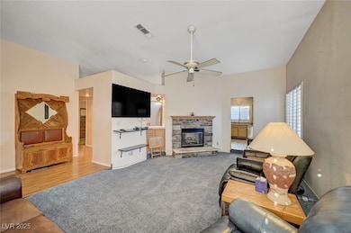 Living room with a stone fireplace, ceiling fan, and light carpet