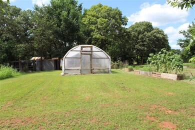 View of yard featuring a greenhouse, a garden, an outbuilding, and view of wooded area