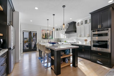 Kitchen with dark cabinets, backsplash, pendant lighting, custom range hood, and light wood finished floors