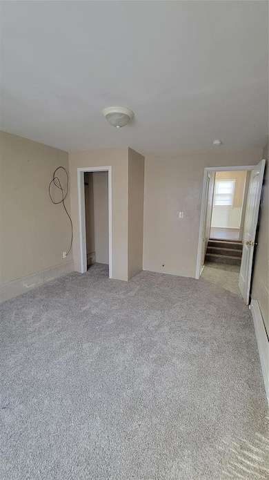 Unfurnished room featuring light carpet, a baseboard heating unit, and stairway