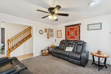 Carpeted living room with stairway and ceiling fan
