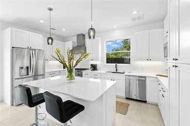 Kitchen featuring appliances with stainless steel finishes, wall chimney range hood, decorative backsplash, light countertops, and a kitchen breakfast bar