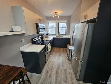Kitchen featuring light countertops, appliances with stainless steel finishes, dark cabinetry, light wood finished floors, and white cabinetry