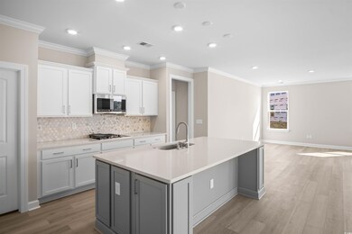 Kitchen featuring gray cabinets, white cabinetry, crown molding, light wood-style floors, and decorative backsplash