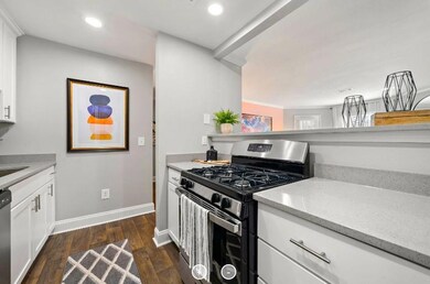Kitchen with dark wood-type flooring, appliances with stainless steel finishes, white cabinets, light stone counters, and sink