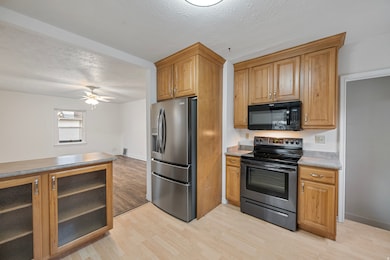Kitchen featuring a textured ceiling, appliances with stainless steel finishes, light wood finished floors, glass insert cabinets, and brown cabinetry
