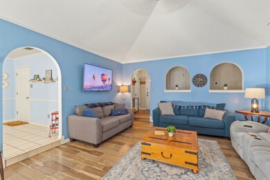 Living area with arched walkways, ornamental molding, lofted ceiling, and wood finished floors