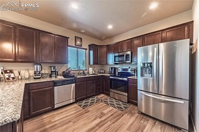 Kitchen with appliances with stainless steel finishes, dark brown cabinets, light wood finished floors, recessed lighting, and light stone countertops