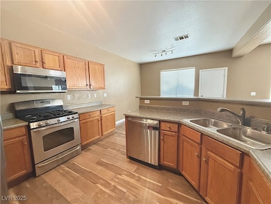 Kitchen featuring stainless steel appliances, light wood-style flooring, a textured ceiling, track lighting, and brown cabinets