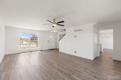 Unfurnished living room featuring wood-type flooring and ceiling fan with notable chandelier