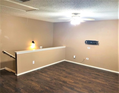 Empty room featuring attic access, wood finished floors, a textured ceiling, and a ceiling fan