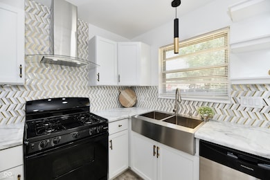 kitchen featuring black gas stove, wall chimney exhaust hood, dishwasher, and white cabinets