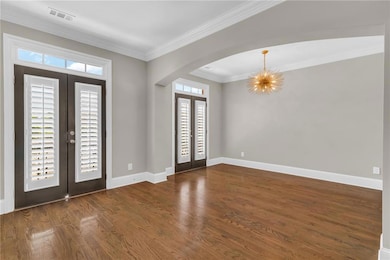 Entrance foyer featuring french doors, arched walkways, ornamental molding, dark wood-style floors, and a chandelier