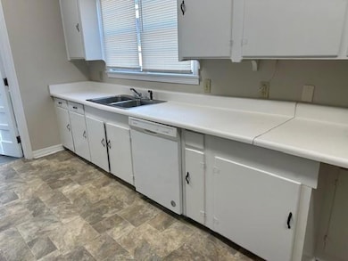 Kitchen with dishwasher, a sink, stone finish flooring, and white cabinets