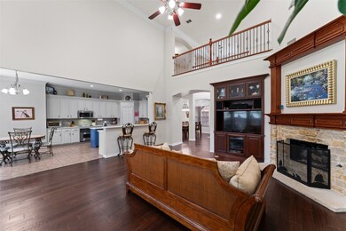 Living room featuring arched walkways, ceiling fan, ornamental molding, wood finished floors, and a stone fireplace