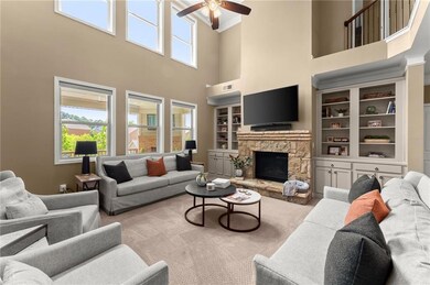 Carpeted living area featuring a high ceiling, ceiling fan, a stone fireplace, and built in features